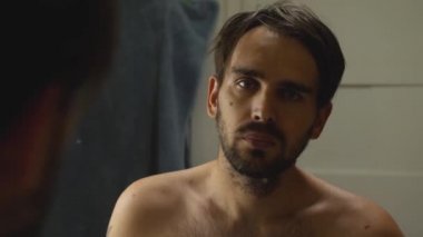 Banyoda gömleksiz bir adam aynada kendine bakar. Bir jilet çıkardı ve onu sakalından geçirdi. Acı içinde çığlık atıyor.