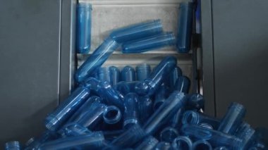 Hopper 'dan gelen mavi preform konveyörden üfleme makinesine gidiyor. Maden suyu şişeleme tesisinde plastik şişe üretimi