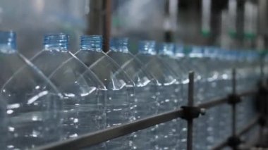 5 litrelik hacimli boş plastik şişeler, maden suyu şişeleme fabrikasının atölyesindeki taşıyıcı boyunca hareket ediyor. Yiyecek işleme tesisinde içme suyu üretimi