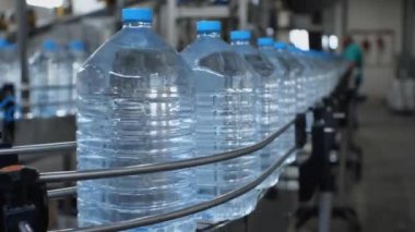 Mavi beş litrelik şişeler gıda endüstrisi fabrikasındaki içme suyu üretimi için dükkandaki taşıyıcıya gidiyor.