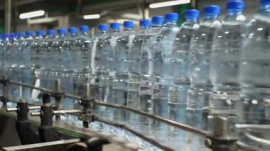 Taşıyıcıya yakın plan, maden suyu ile plastik şişeleri hareket ettiriyor. Yiyecek işleme tesisinde içme suyu üretimi