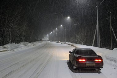 Karlı bir gece otoyolunda fenerlerin ışığında bir araba. Kış Yolculuğu Konsepti