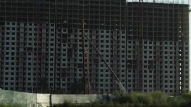 Çok katlı bir binanın inşaatı. Çok katlı vinçler ve insanlar kadrajda. Kamera aşağıdan yukarıya doğru hareket ediyor. Uygun fiyatlı konut inşaatı kavramı