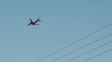 Uçak iniş için arka plandaki elektrik hatlarına ve mavi gökyüzüne doğru geliyor. Alt kenar görünümü
