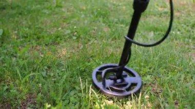 Bir metal detektörü hazine araması için yeşil çimlerin üzerinde sağa sola hareket ediyor.