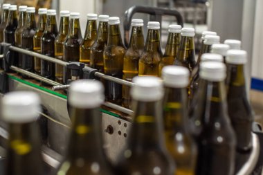 Üretim salonundaki taşıyıcı bantta kahverengi cam su şişeleri var. Gıda üretimi