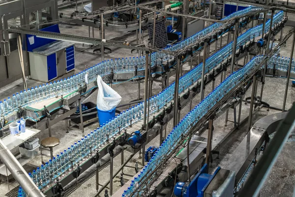 Bir maden suyu üretim atölyesinde mavi plastik içme suyu şişeleri ile konveyör hattı. Gıda üretimi