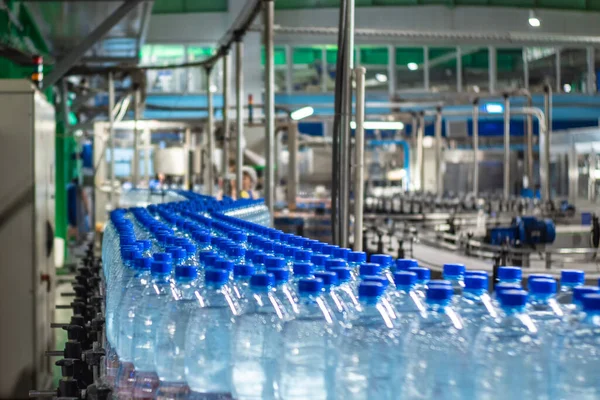 Blue plastic bottles in three rows with clean drinking water on a conveyor belt at a mineral water plant. Food production