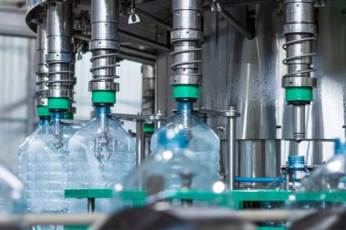 İçme suyunu beş litrelik plastik şişelerde şişelemek için otomatik hat. Şişeyi otomatik dolgu makinesiyle doldurma işlemi. Gıda üretimi