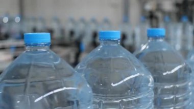 Taşıyıcı boyunca hareket eden beş litrelik su şişelerinin yakın çekimi. Fabrikada içme suyu üretim hattı