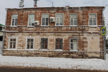Kliması ve buz saçakları olan eski bir tuğla bina. Gri bir kış şehri