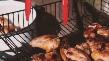 Kırmızı mutfak maşası ızgaradaki tavuk kanatlarını al ve tencereye koy. Çok lezzetli tavuk eti. Yakın plan. Açık hava yemekleri kavramı.