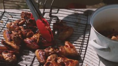 Kızarmış tavuk kanatlarını ızgaradan alıp tencereye koyan kırmızı mutfak maşası yakın plan. Çok lezzetli tavuk eti. Açık hava yemekleri kavramı.