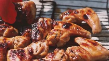 Kızarmış tavuk kanatlarını ızgaradan çıkaran kırmızı mutfak maşası yakın plan. Çok lezzetli tavuk eti. Açık hava yemekleri kavramı.