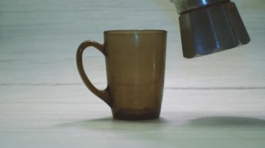 Kahve gayzer kahve makinesinden siyah cam bardağa, açık arkaplana dökülüyor. Evde lezzetli kahve yapma süreci..