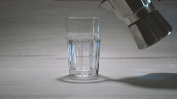 Dans une tasse en verre clair debout sur un fond clair, le café est versé à partir d'une cafetière geyser. Le processus de fabrication de délicieux café à la maison. — Video