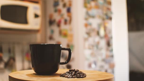 Een Zwarte Mok Een Handvol Gebrande Koffiebonen Tegen Een Keukeninterieur — Stockvideo
