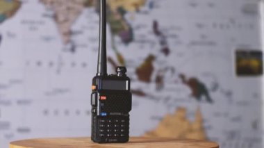 Bulanık bir dünya haritasının arka planında siyah taşınabilir radyo vericisi Baofeng UV-5R var. Kamera etrafta uçuyor. Parallaks etkisi. Krasnodar, Rusya 9 Eylül 2021