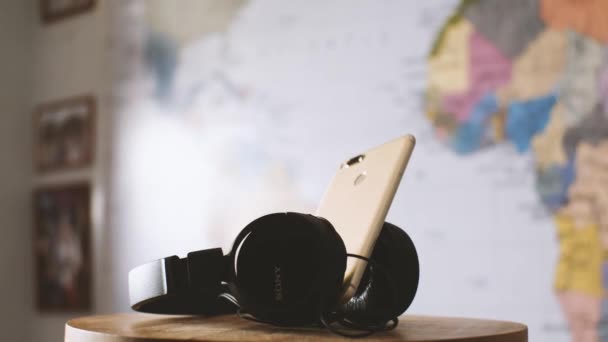 大きな黒い有線ソニーのヘッドフォンとぼやけた世界地図に対するXiaomiのスマートフォン カメラが飛び回っている パララックス効果 スローモーション ロシアのクラスノダール2021年9月9日 — ストック動画