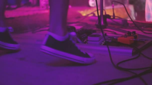 ギタリストのスニーカーの足は エレキギターのためのギタープロセッサ プライマー および他の電子機器の前でバウンス 多色舞台照明作品 — ストック動画
