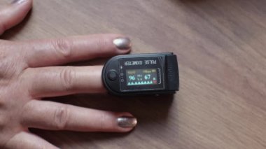 Yaşlı bir kadın kan ve nabız doygunluğunu oksimetrenin yardımıyla ölçer. Okumalar LCD ekranında gösteriliyor. Kendi sağlığını gözlemlemek.