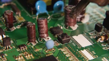 Usta bir tamirci elektronik devre kartındaki çipi çıkarmak için lehimleme istasyonu ve cımbız kullanıyor. Yakın plan. Elektronik, bilgisayar, telefon ve televizyon tamirhanesi