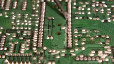 Tamir teknisyeni lehim iğnelerini yeşil akı elektronik paneline yağlıyor. Yakın plan. Elektronik, bilgisayar, telefon ve televizyon tamirhanesi