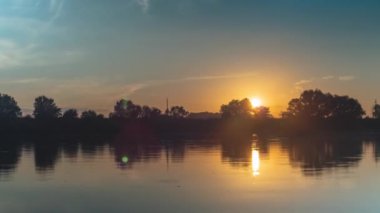 Nehrin üzerinde gün batımı. Ağaçlar ve bulutlar suya yansıyor. Hafifçe kameraya yakınlaşıp uzaklaşıyor. Doğanın bir zamanı.