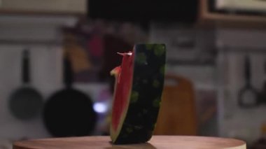 Kemikli kırmızı bir karpuz dilimi kesme tahtasının üzerinde duruyor. Kamera etrafta uçuyor. Parallaks etkisi