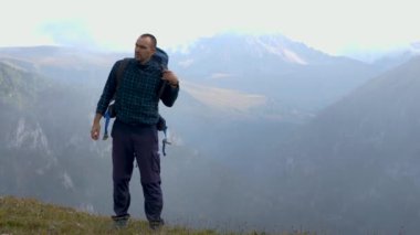 Ekose yün ceketli bir erkek yürüyüşçü sırt çantasını sırtından çıkarıyor. Arka planda bir vadi ve karlı dağ tepeleri var. Yürüyüş konsepti