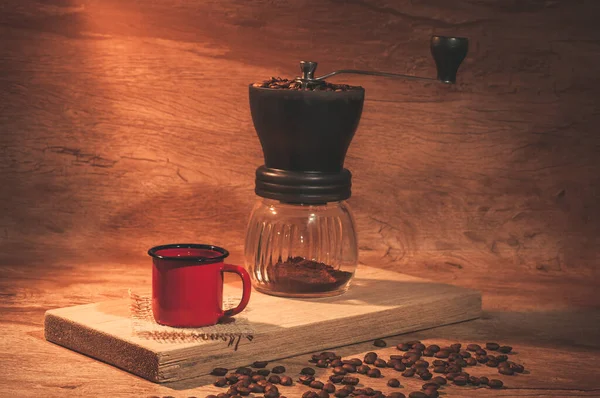 Red coffee mug with coffee grinder in the background. Rustic wooden background.