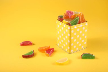 çok renkli marmelat turuncu dilimler şeklinde sarı arka planda kare bir kasede.