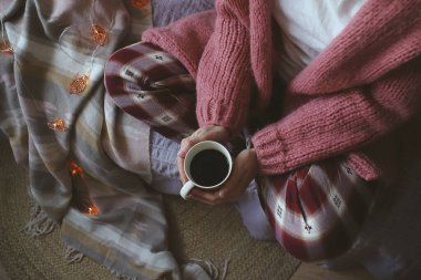 Süveter giymiş bir kadın eli bir kupa kahve tutuyor. Noel süslemesi.