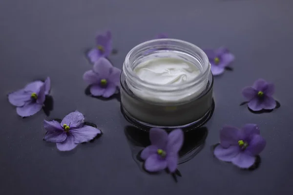 white jar with cream on a background with water decorated with purple violets