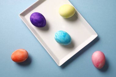 Mavi arka planda beyaz tabakta renkli paskalya yumurtaları.