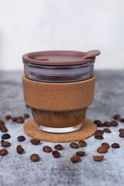 Gri arka planda tekrar kullanılabilen kahve fincanı. Çevre koruma kavramı, doğayı kurtarma, sıfır atık. Plastik kirliliğe yol açmaz. Kahve molası. Camdan ve mantardan yapılmış kupayı almak için.