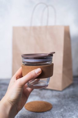 Gri arka plan biyoloji paketinin üzerinde kadınlar tarafından yeniden kullanılabilir kahve fincanı tutuluyor. Çevre koruma kavramı, doğayı kurtarma, sıfır atık. Plastik yok. Paket cam bardak..