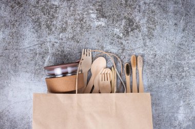 Temel çevre dostu bambu takımları, yeniden kullanılabilir kahve fincanları, diş fırçaları, kağıt alışveriş torbası üzerindeki metal tüpler, gri arka plan. Çevre koruma kavramı, plastiksiz, sıfır atık. Boşluğu kopyala
