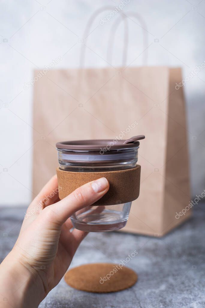 Womens hand hold eco reusable coffee cup on the gray background craft bio package. Concept of environmental protection, save nature, zero waste. No plastic. Takeaway glass mug.