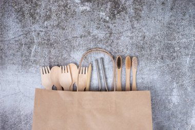Temel çevre dostu yeniden kullanılabilir bambu takımları, diş fırçaları, kağıt alışveriş torbası üzerindeki metal tüpler, gri arka plan. Çevre koruma kavramı, plastiksiz, sıfır atık. Boşluğu kopyala