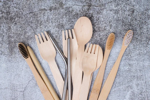 Basic set eco friendly reusable bamboo cutlery, toothbrushes, metal tubes on gray background close up. Concept of environmental protection, plastic free, zero waste. Minimalistic life