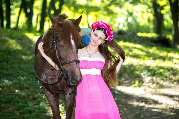 Beautiful girl in long pink dress near big brown horse — Stock Photo, Image