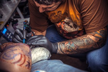 Tattooist makes tattoo in tatoo salon clipart