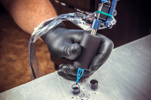 Artista de tatoo trabalhando com uma máquina de tatoo com luvas pretas e use tintas pretas para tatuar . — Fotografia de Stock