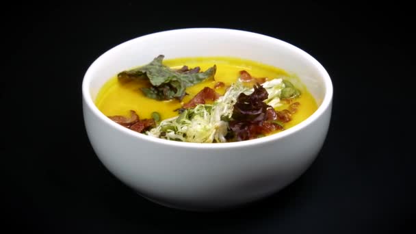 Yellow soup with slices of bacon and lettuce in a white bowl on the black background — Stock Footage Yellow soup with slices of bacon and lettuce in a white bowl on the black background Stock Video