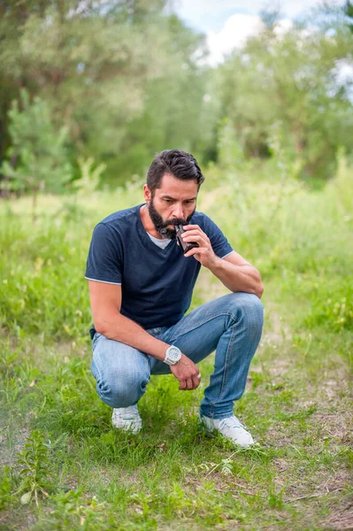 L'uomo barbuto elegante sta riposando in natura e vaporizzando e sfogandosi da una sigaretta elettronica. Non fumatori di tabacco. — Foto Stock