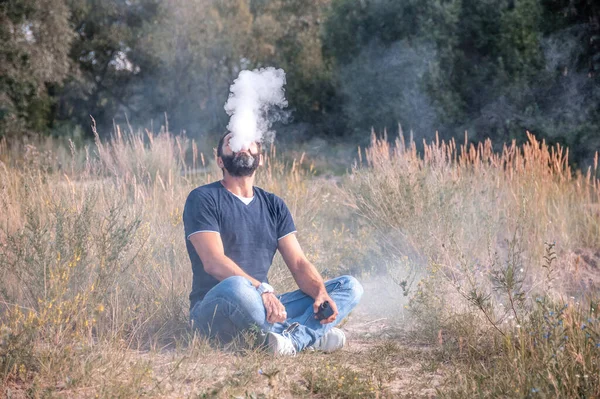 Modern Vaper orman zemininde bir tencerenin tadını çıkarıyor. Adam sigara içiyor.. — Stok fotoğraf