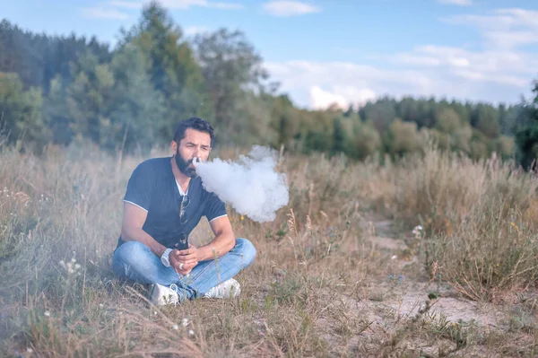 Un moderno vaper rilascia una nuvola di vapore nella foresta. Sigaretta elettronica concetto. — Foto Stock