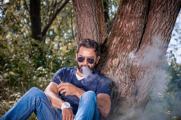 Fumatore barbuto che si gode una sigaretta elettronica nella calma all'aperto. Sigaretta ibrida. — Foto Stock