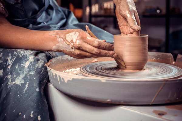 Close-up A woman potter in beautifully sculpts a deep bowl of brown clay and cuts off excess clay on a potters wheel in a beautiful workshop